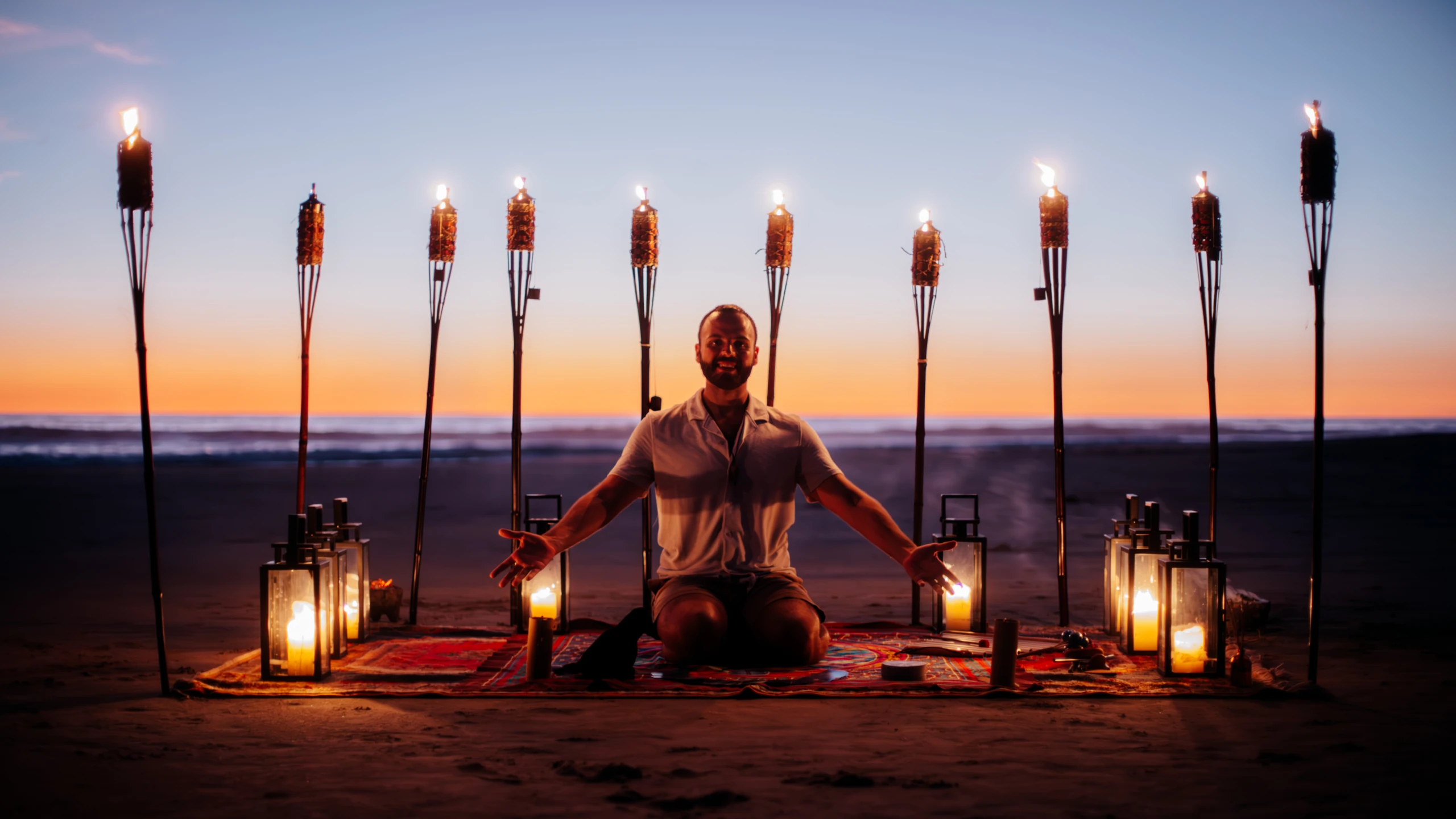 SANTOS seated on a beach at sunset among torches