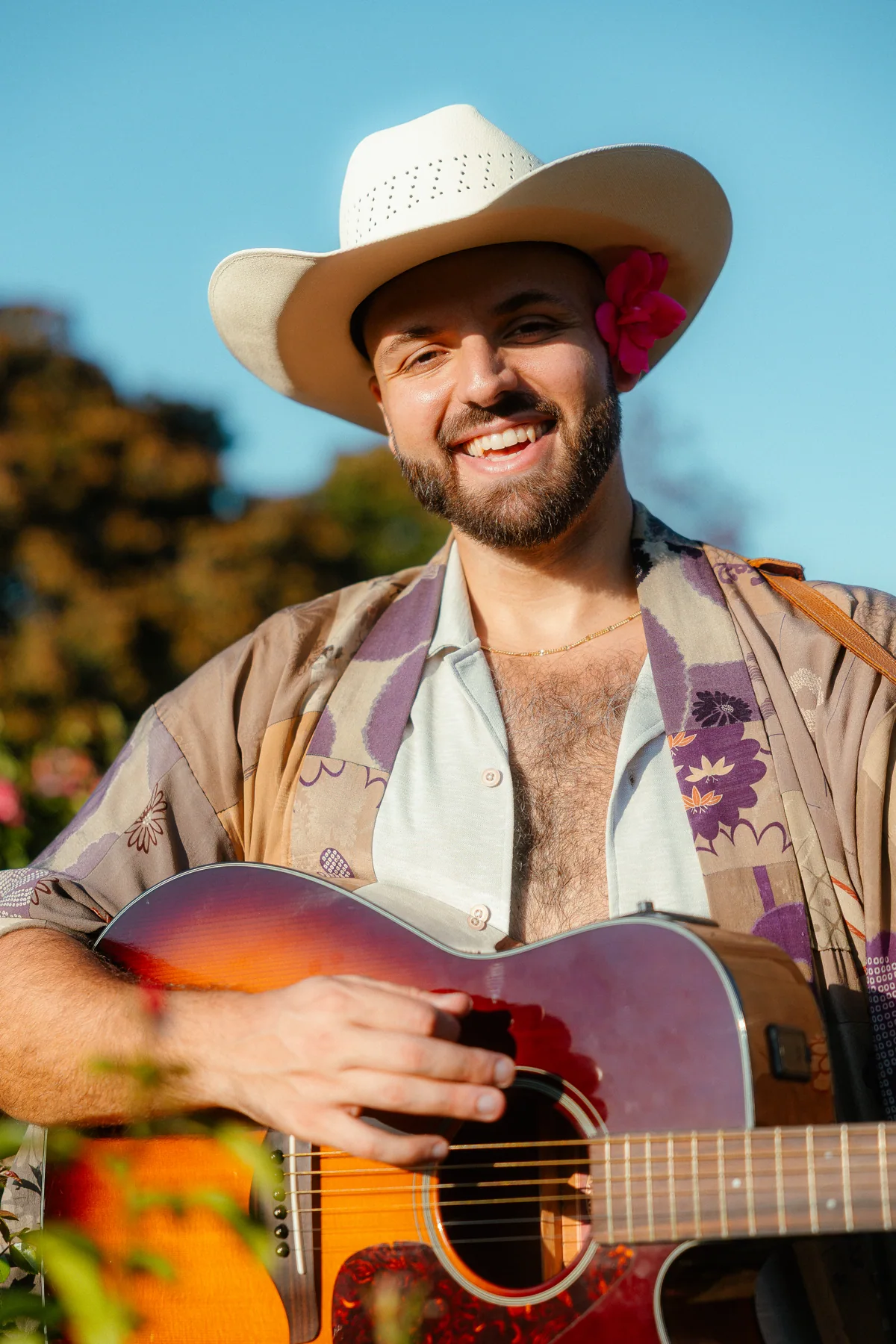 SANTOS smiling with a guitar in the rose garden