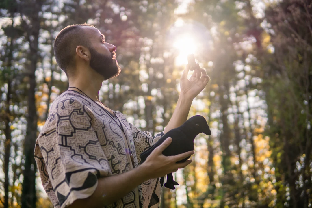 SANTOS holding a crow figure in a woodland setting