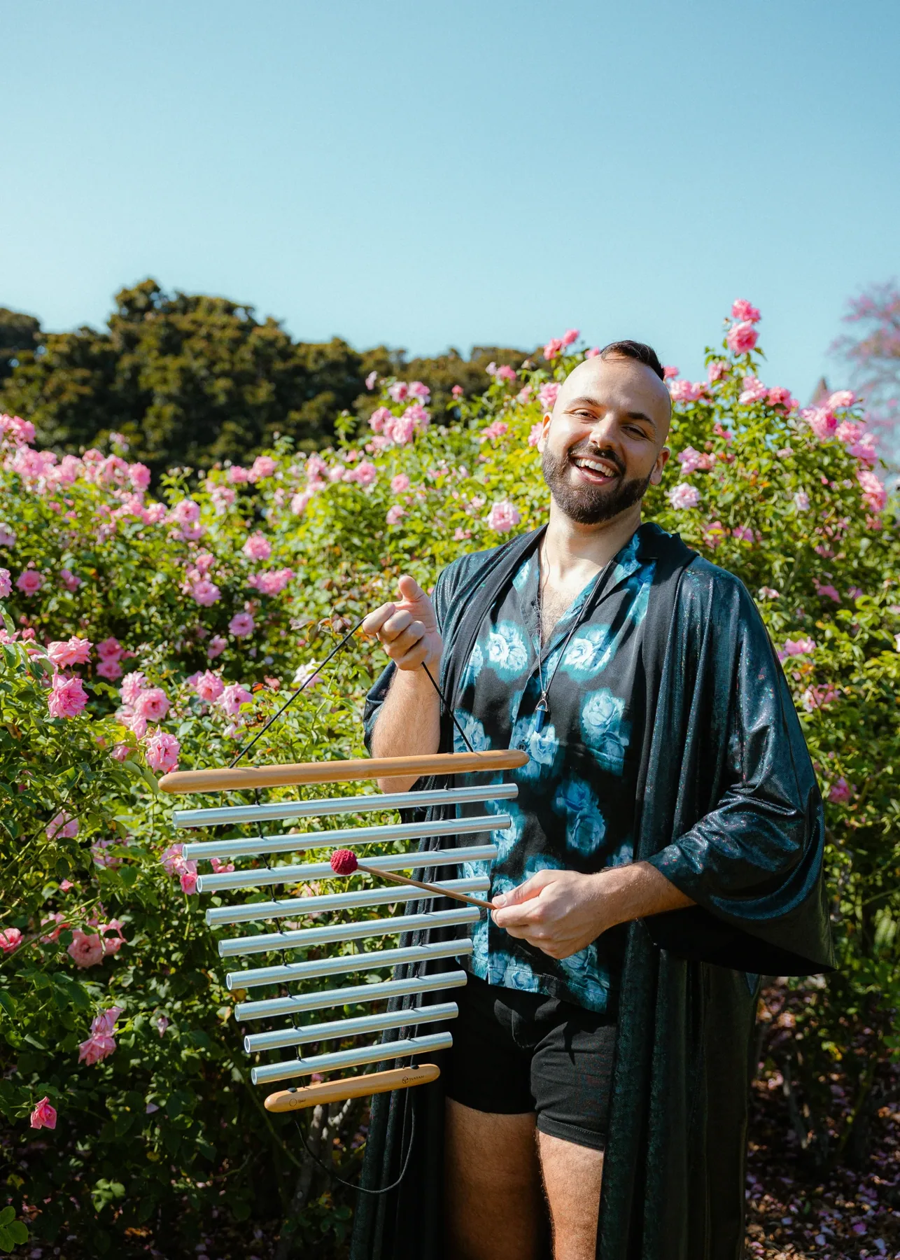 SANTOS holding chimes in a flower-filled garden